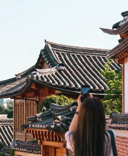 Tourist taking photo of traditional Korean hanok architecture with curved tile rooftops and wooden structures